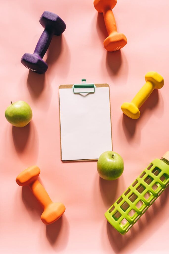 pexels-photo-8155156 Flat lay of gym weights, apples, clipboard, and water bottle on peach background.